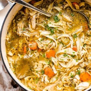 overhead shot of chicken noodle soup in a white dutch oven with a ladle inside the pot