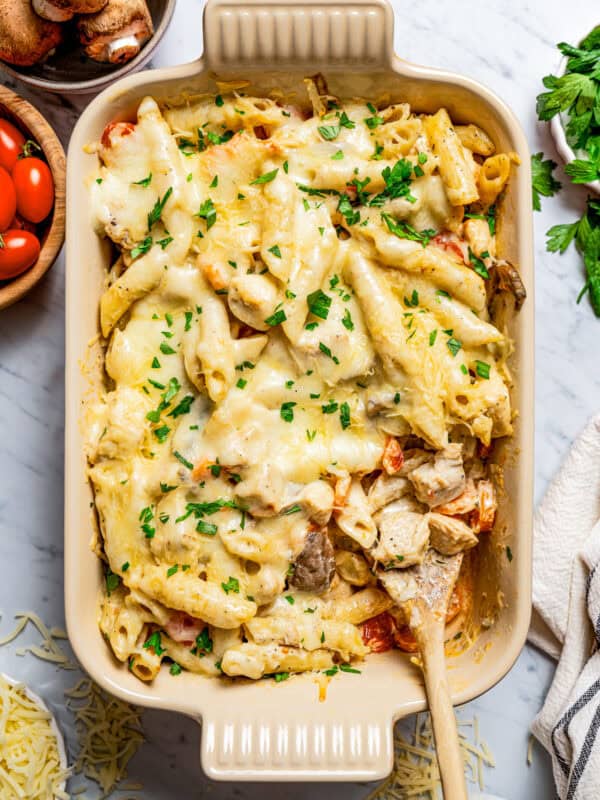 Overhead view of chicken pasta casserole garnished with parsley, with a wooden spoon.