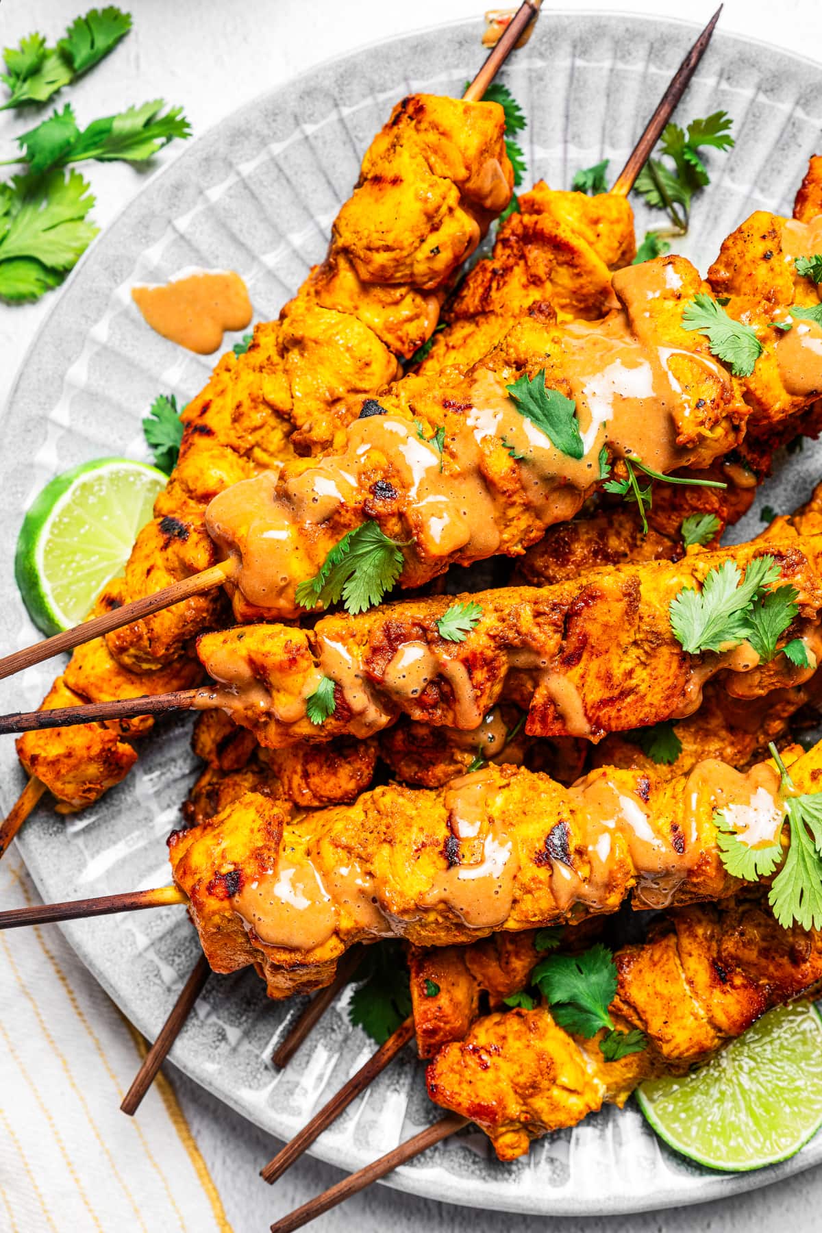 Chicken satay skewers drizzled with peanut dipping sauce and garnished with cilantro.