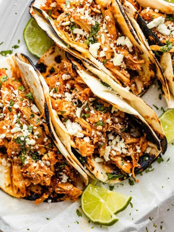 four chicken tinga tacos arranged on a plate and topped with cheese