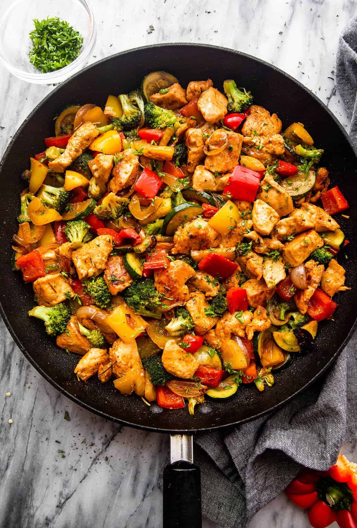 overhead shot of cut up chicken breast cooked in a skillet with zucchini, broccoli, and bell peppers