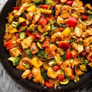 overhead shot of cut up chicken breast cooked in a skillet with zucchini, broccoli, and bell peppers