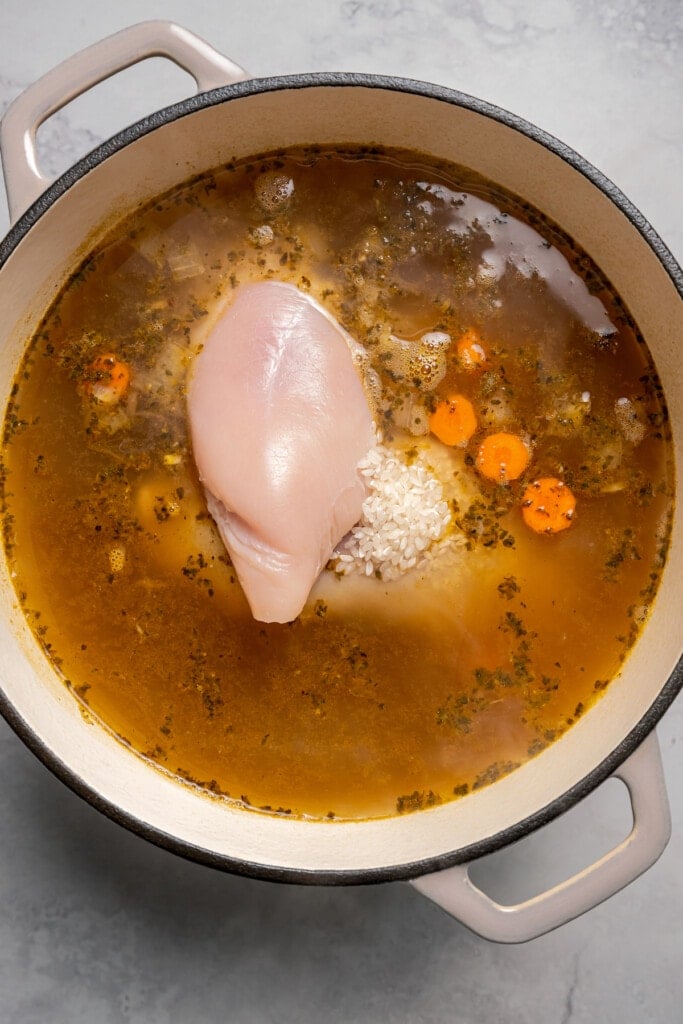 Adding chicken and rice to a soup pot full of veggies and stock.