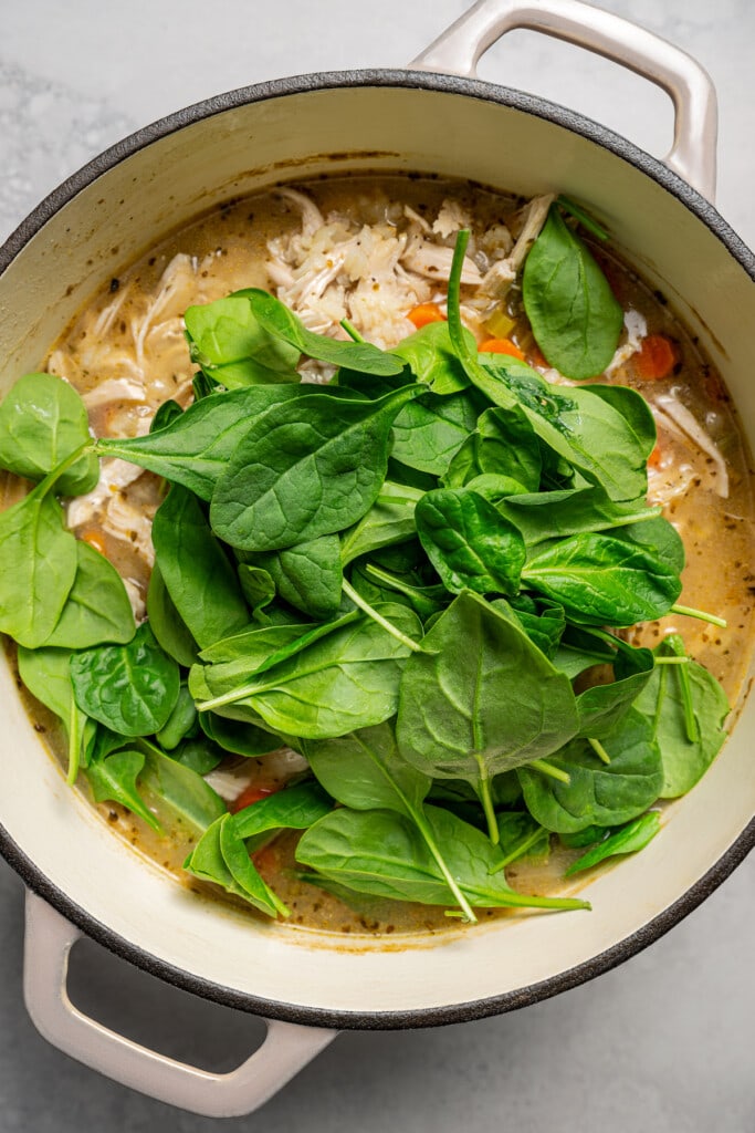 Adding baby spinach to chicken and vegetable soup.