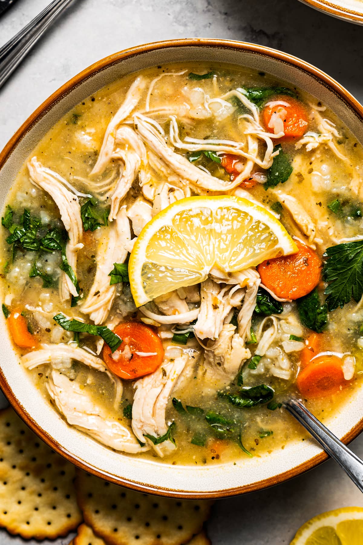 Closeup overhead image of a bowl of chicken vegetable soup with a spoon in it.