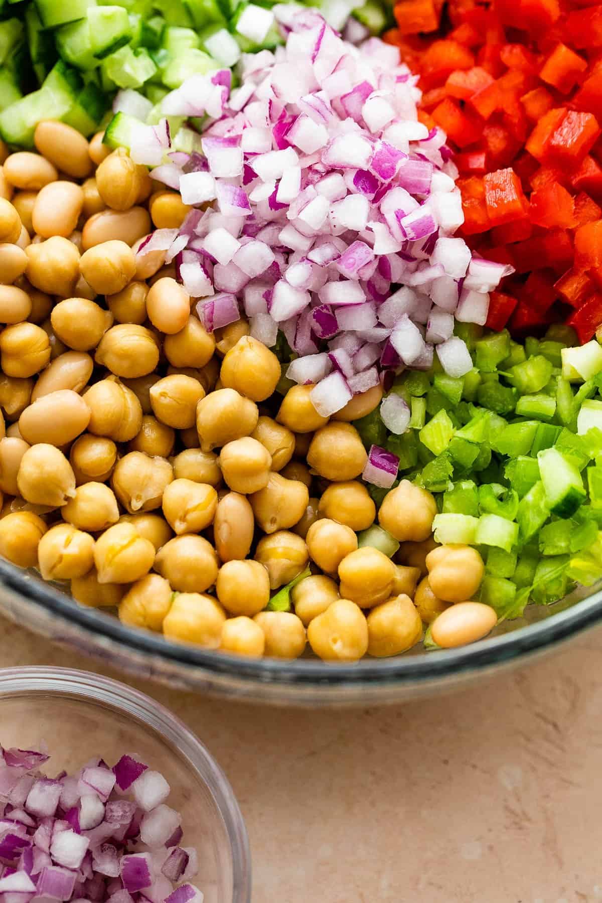 Chickpeas, diced cucumbers, onions, and veggies arranged in a glass salad bowl.