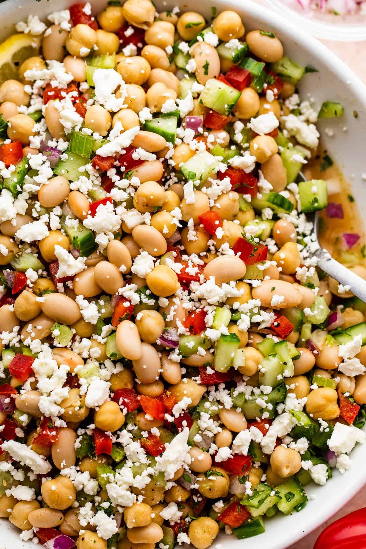 Overhead close-up shot of a white salad bowl with chickpea salad topped with crumbled feta cheese.