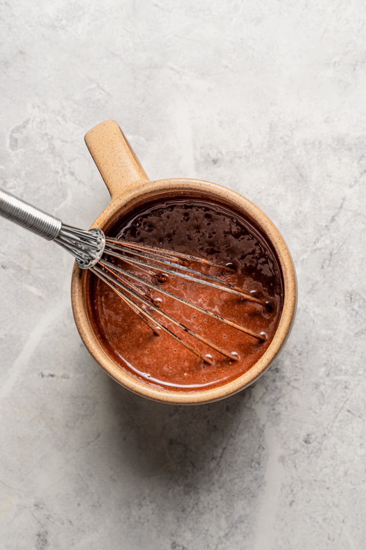 Chocolate cake batter in a mug with a whisk.