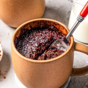 A spoon in a chocolate mug cake, with a second mug cake in the background.