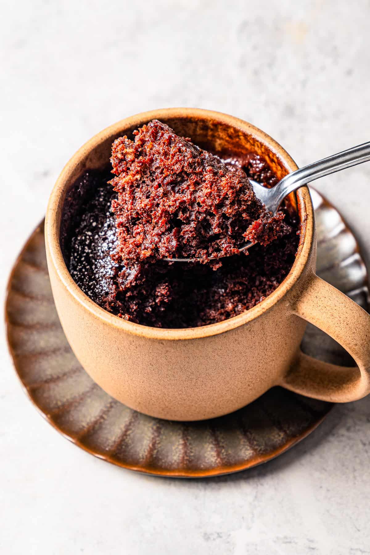 A spoonful of chocolate cake held over a mug.