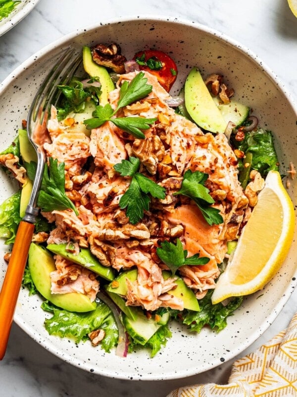 Close-up of a salmon salad in a bowl with salad greens, tomatoes, and a wedge of lemon.