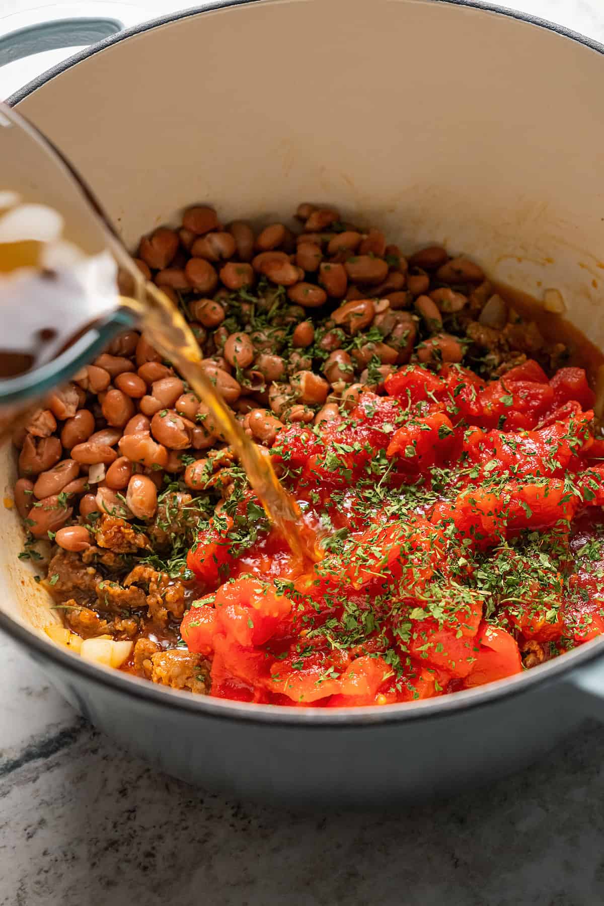 Broth, beans, and tomatoes added to a soup pot with chorizo and onions.