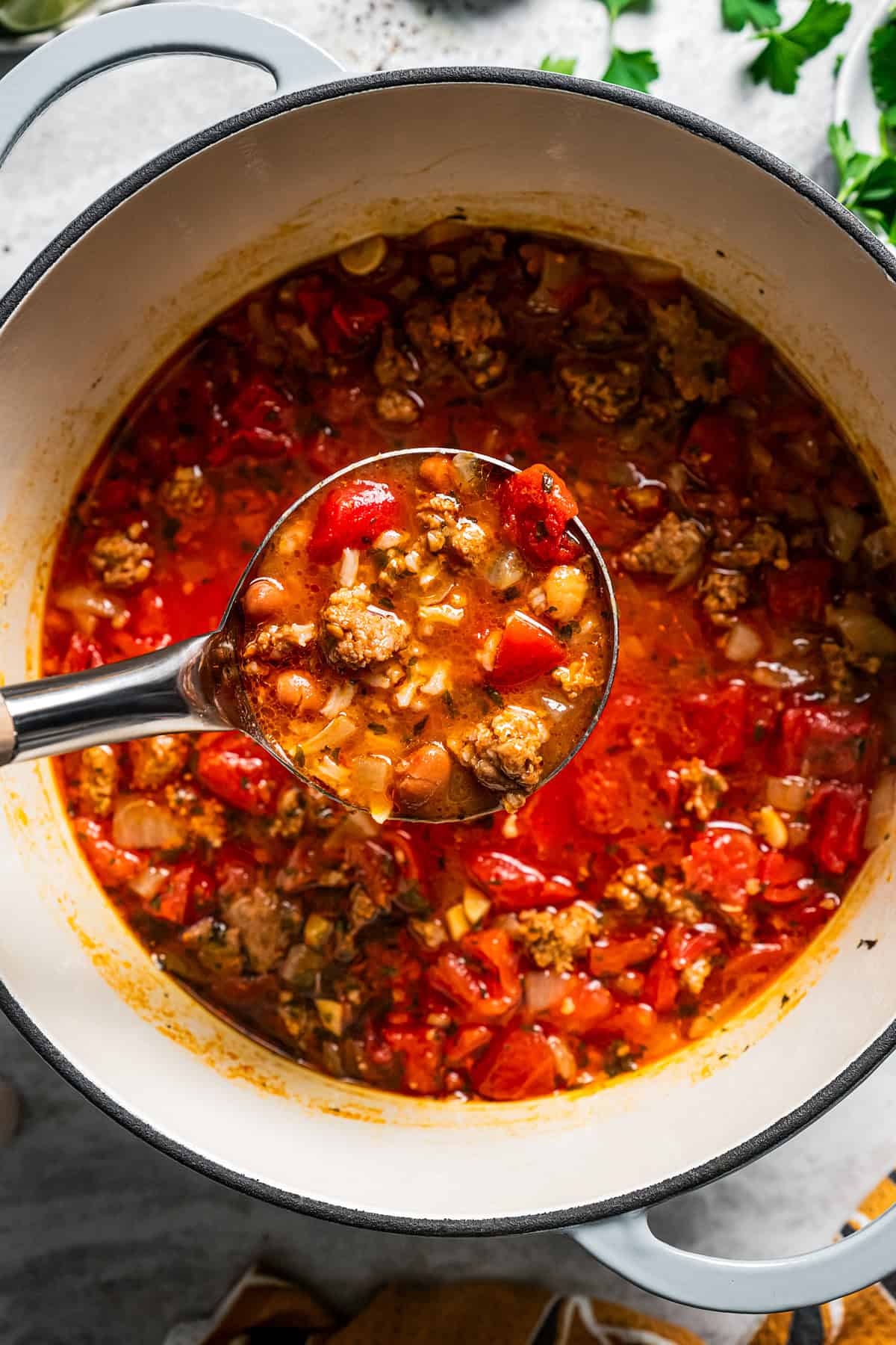 Overhead view of a ladleful of chorizo soup held over a large pot.