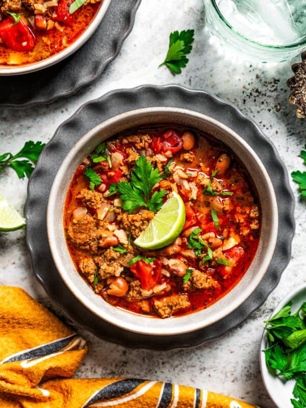 Overhead view of a bowls of chorizo soup garnished with a lime wedge and fresh cilantro, next to a glass of water.