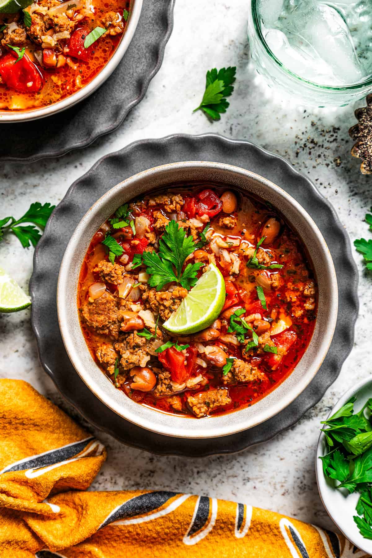 Overhead view of a bowls of chorizo soup garnished with a lime wedge and fresh cilantro, next to a glass of water.