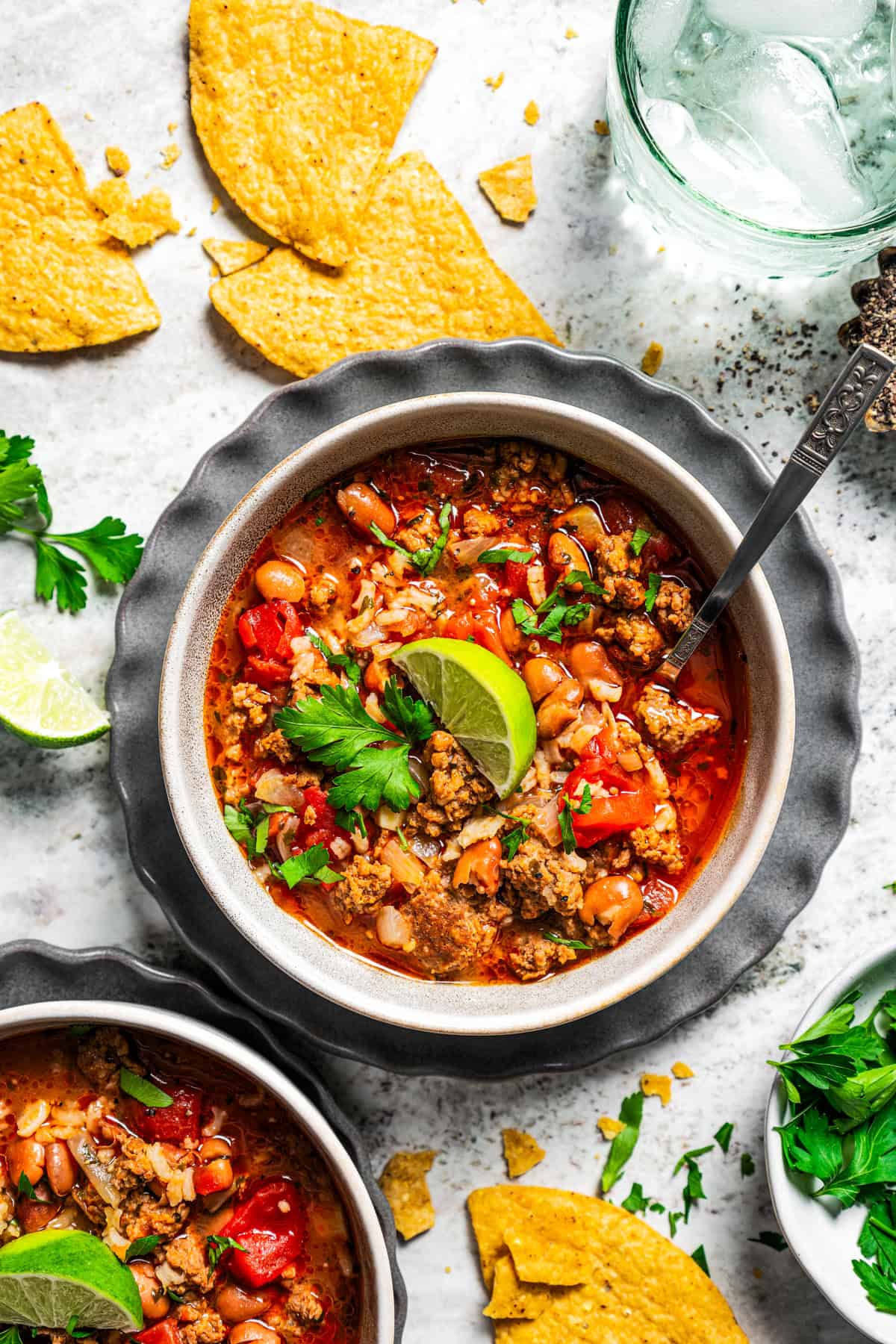 Overhead view of a bowl of chorizo soup garnished with a lime wedge and fresh cilantro, next to a glass of water.