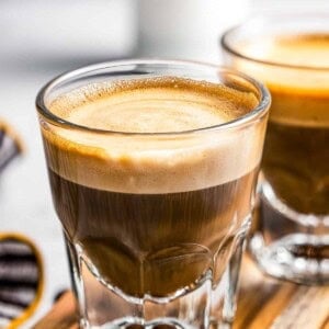 Side shot of two coffee glass mugs filled with cortado coffee.