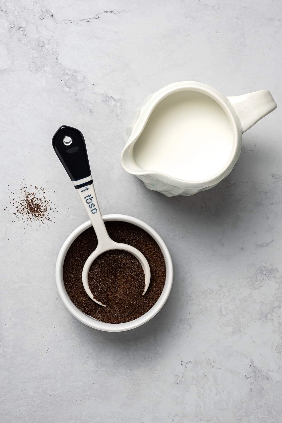 A small pitcher of cream and a bowl with espresso granules and a scoop