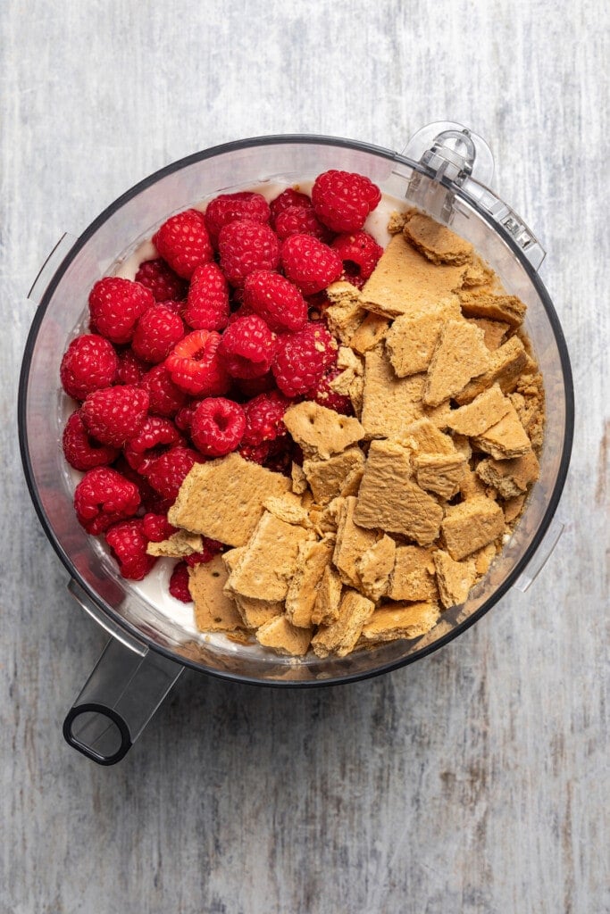 Adding graham crackers and raspberries to a blender full of cottage cheese ice cream.