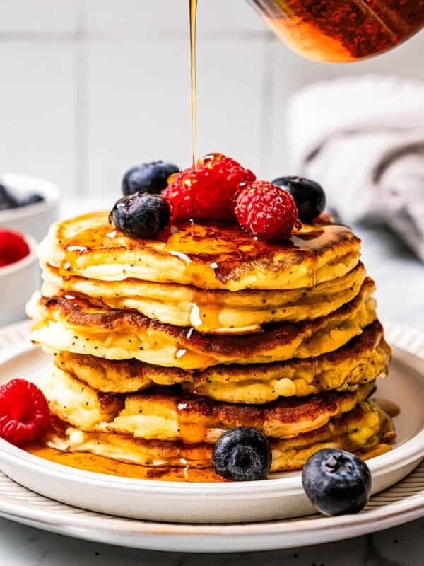 Pouring maple syrup over a stack of cottage cheese pancakes.