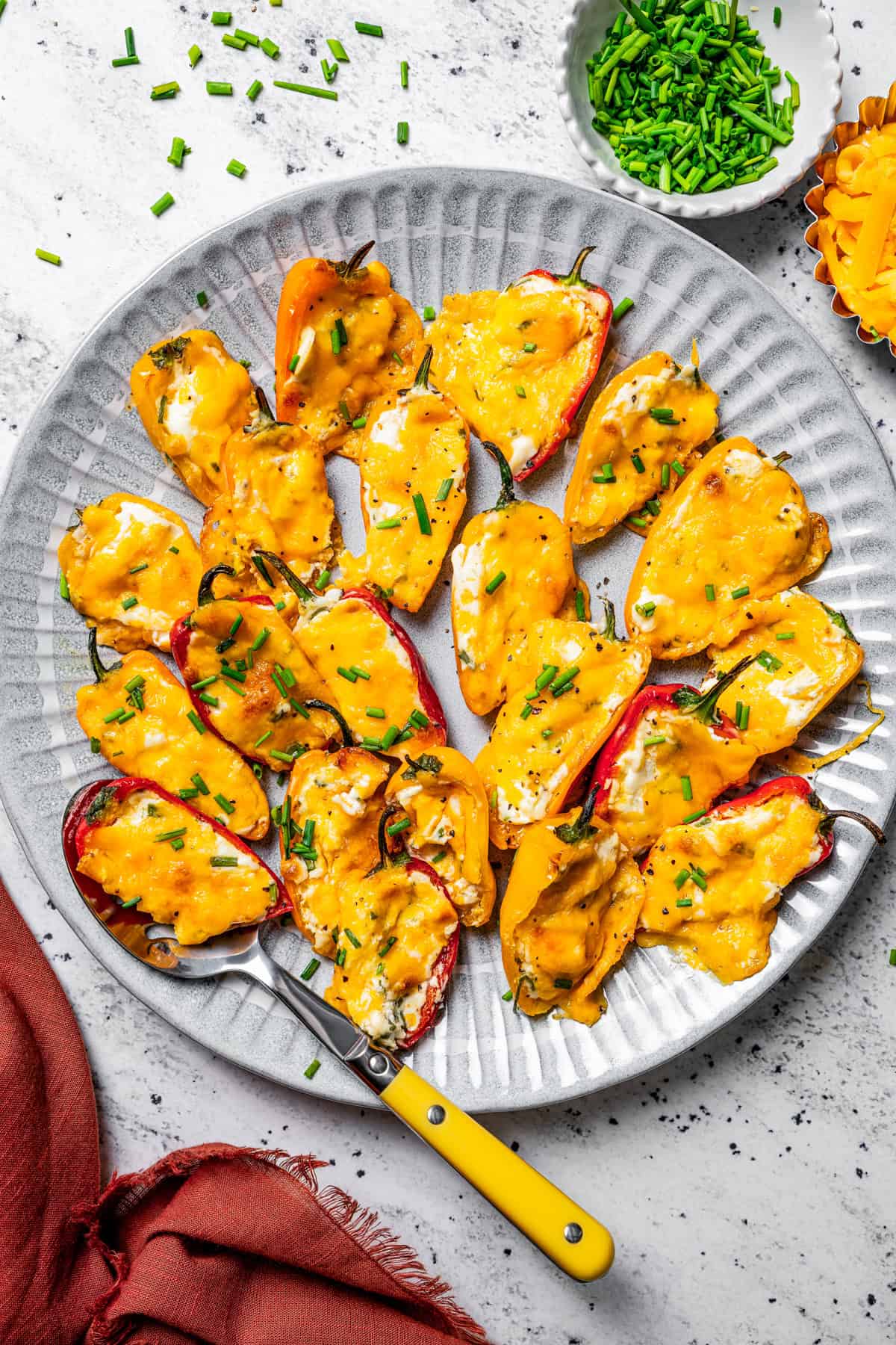 Overhead view of cream cheese stuffed peppers arranged on a plate with a spoon for serving.