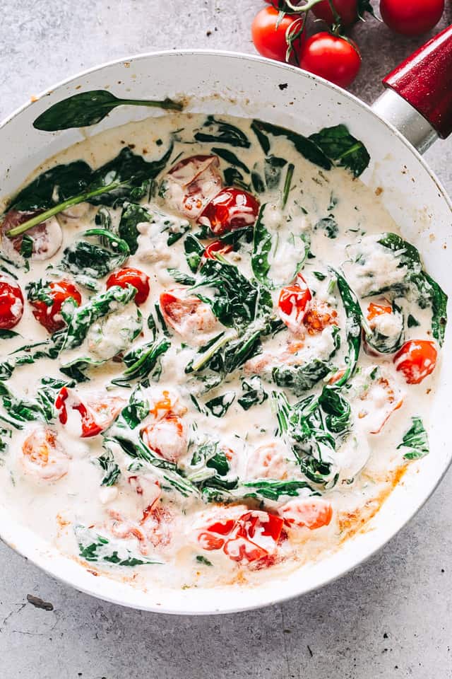 Overhead image of creamy sauce with tomatoes and spinach cooking in a skillet.