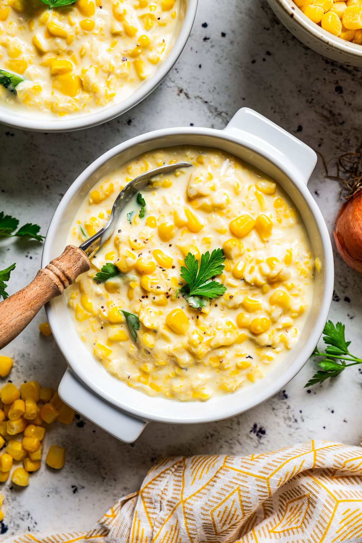 Creamed corn served in white bowls, garnished with fresh green herbs.