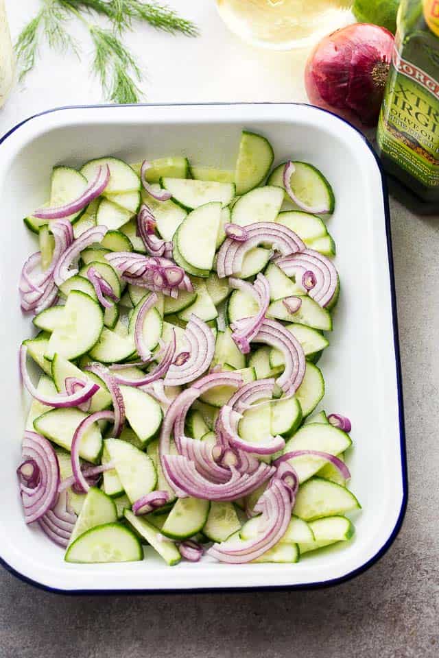 Slices of cucumbers and onions tossed together in a white dish.