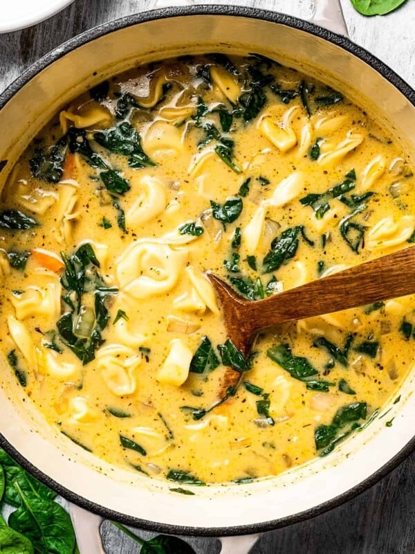 Creamy tortellini soup ingredients simmering in a pot with a wooden spoon.