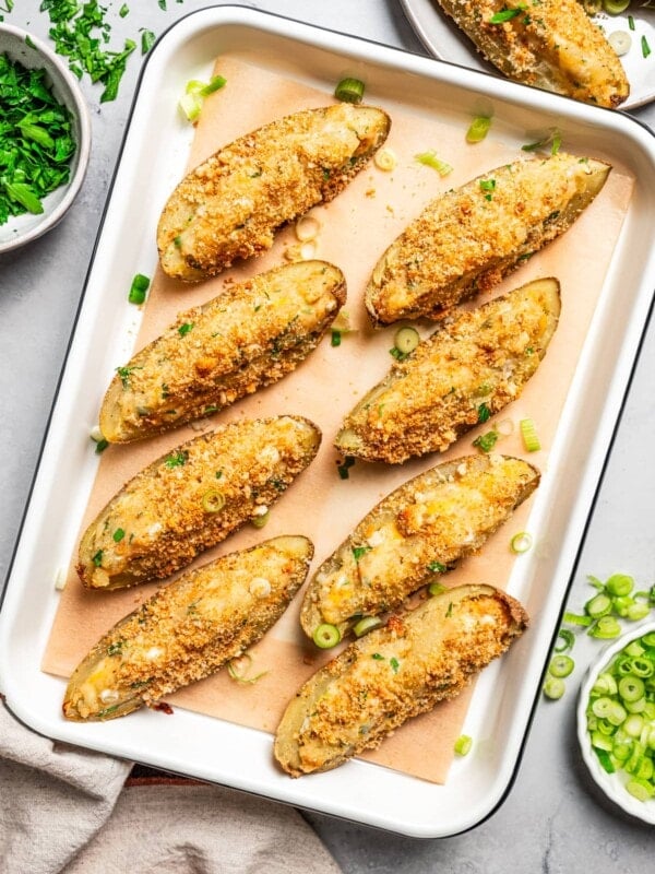 Overhead photo of crispy potato skins topped with crushed croutons and arranged on a baking sheet.