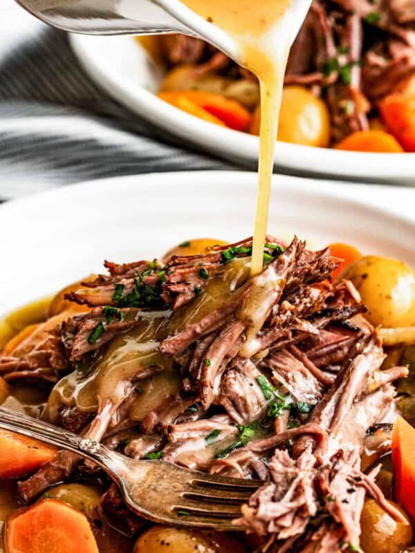 Pouring gravy over crock pot rump roast on a plate with a fork.