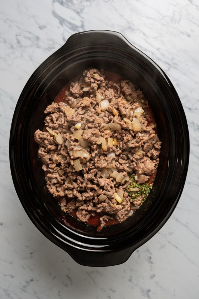 Adding sauteed onions and garlic and browned meat to a crockpot.