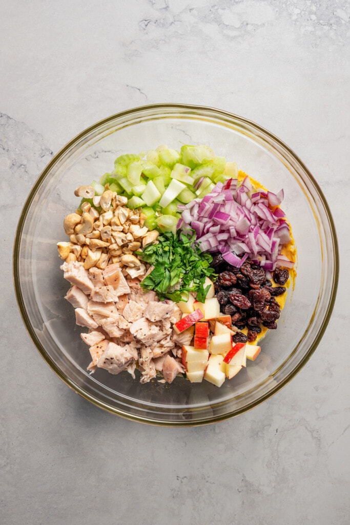 Adding all of the ingredients for curry chicken salad to a bowl.