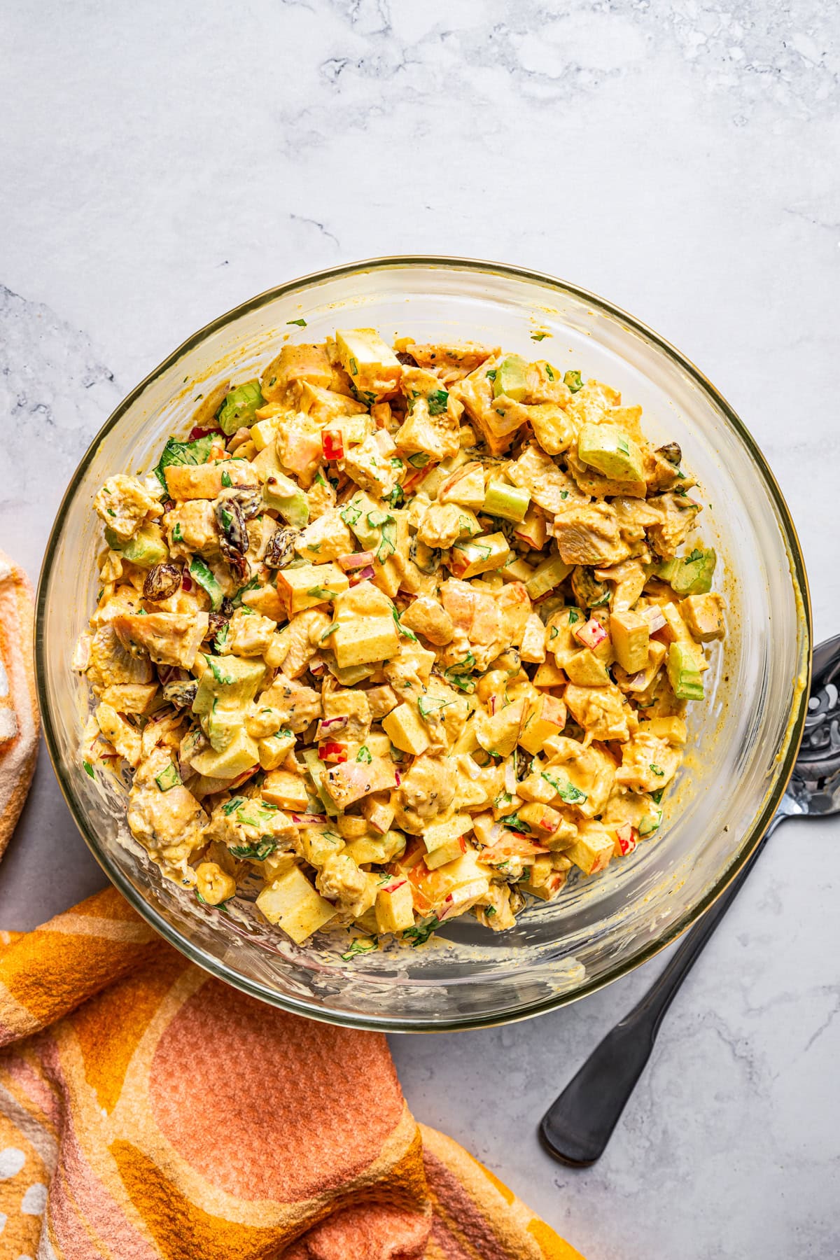 Salad with chicken bites, raisins, chopped apples, and celery in a glass bowl.