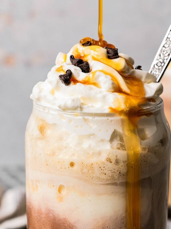 Close-up image of an ice coffee in a glass mug and topped with whipped cream, chocolate chips, and a caramel drizzle.