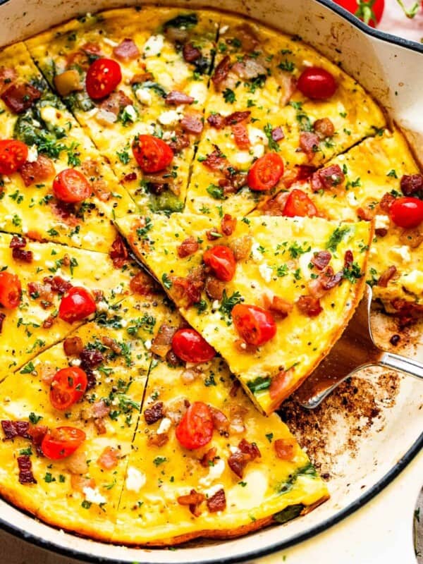 overhead shot of a sliced frittata in a white skillet topped with bacon and tomatoes