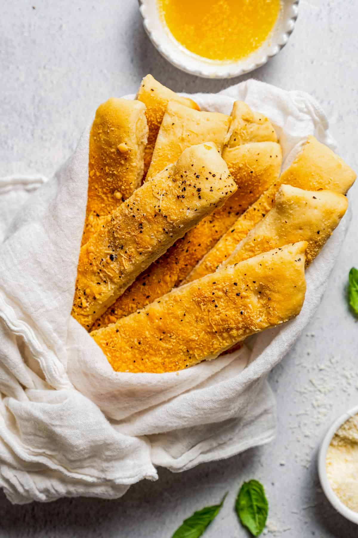 Garlic breadsticks wrapped with a white cloth, next to a bowl of garlic dipping sauce.