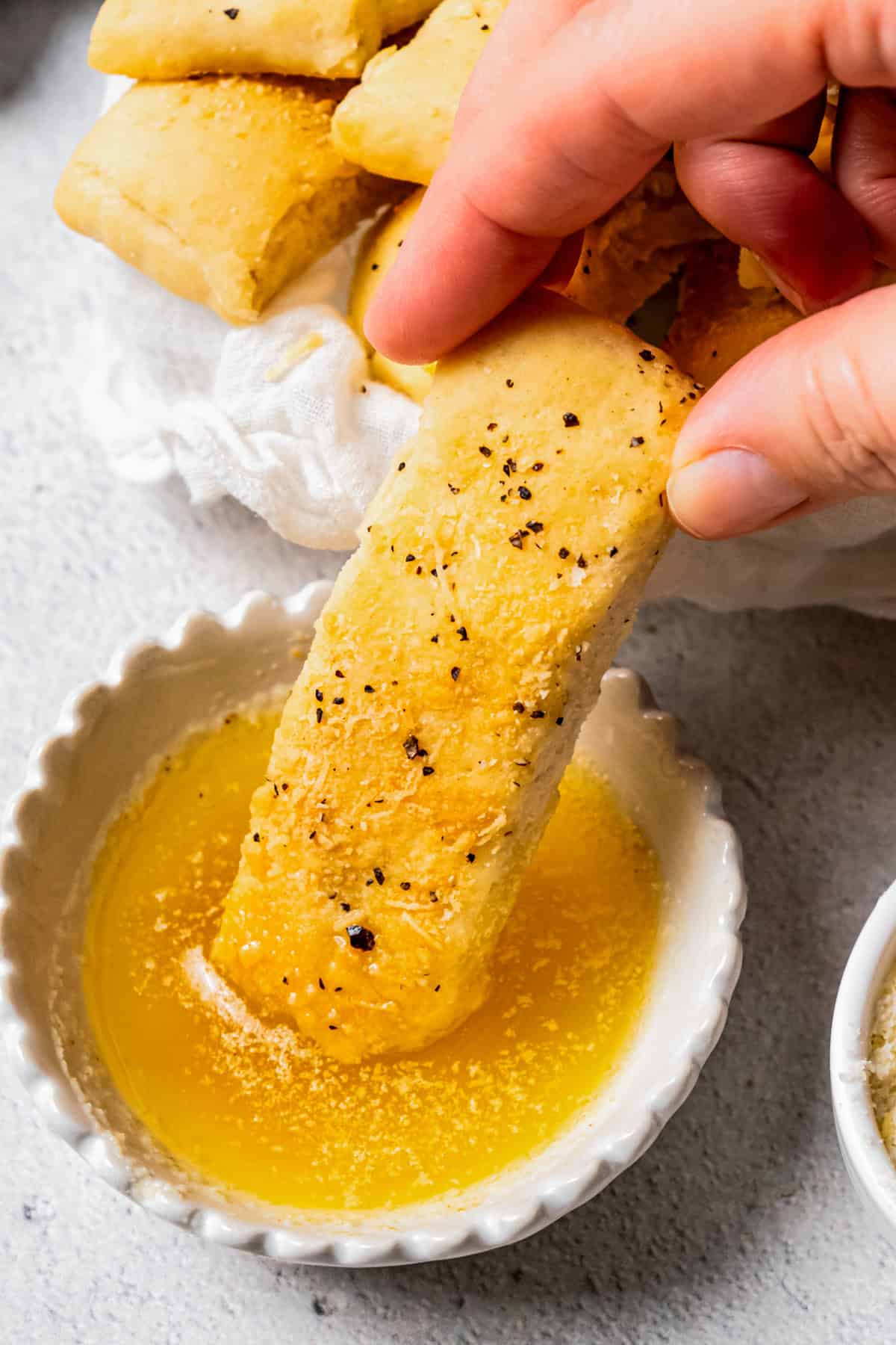 A hand dipping a breadstick into a small ramekin of garlic dipping sauce.