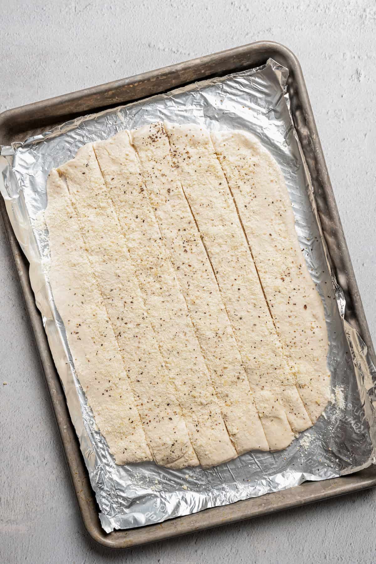 Flattened dough cut into strips on a foil-lined baking tray.