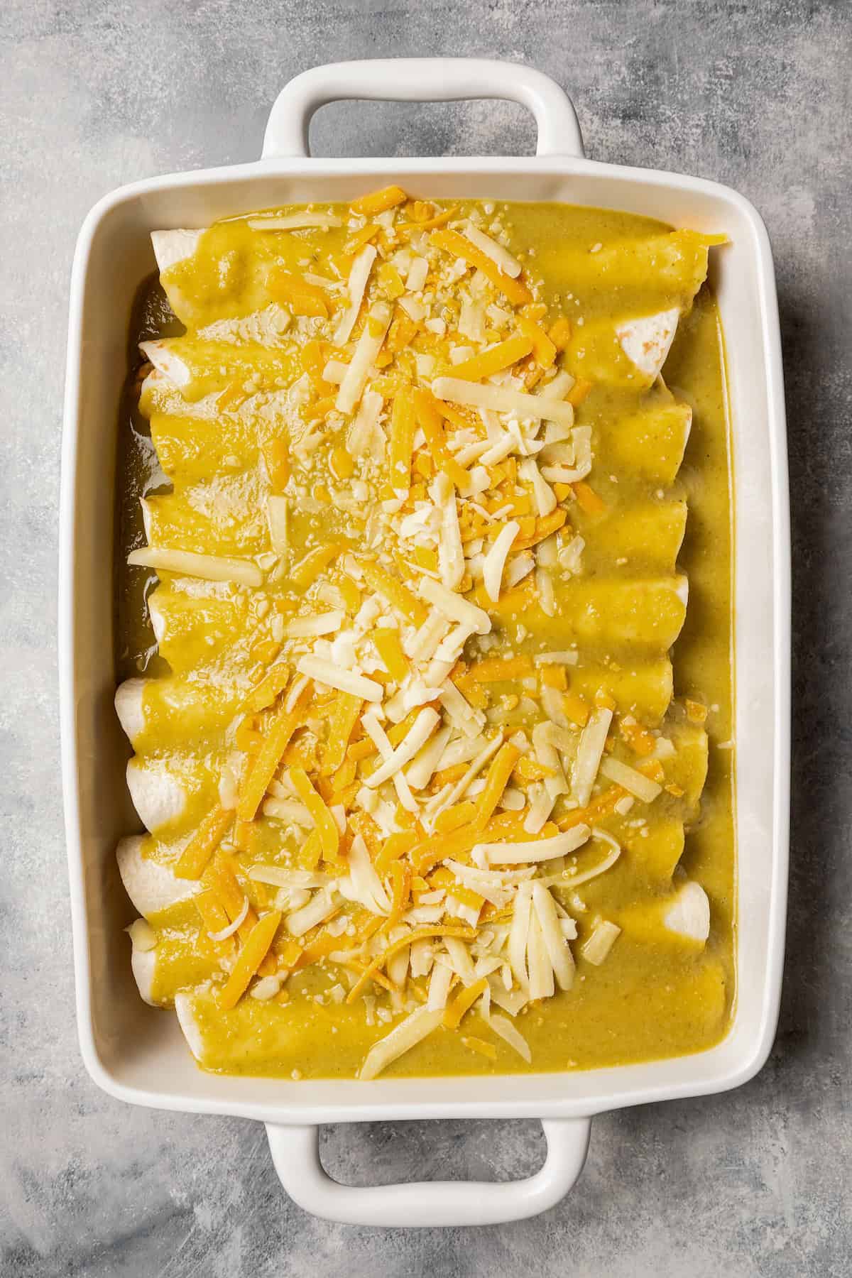 Assembled green chili chicken enchiladas inside a baking dish.