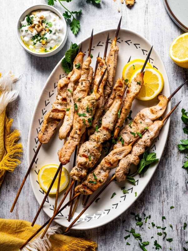 A serving plate with cooked chicken skewers and lemon wedges