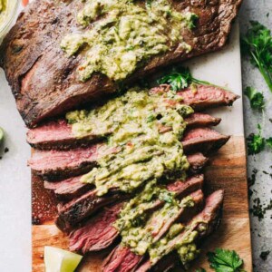 Grilled flank steak with chimichurri sauce on a cutting board.