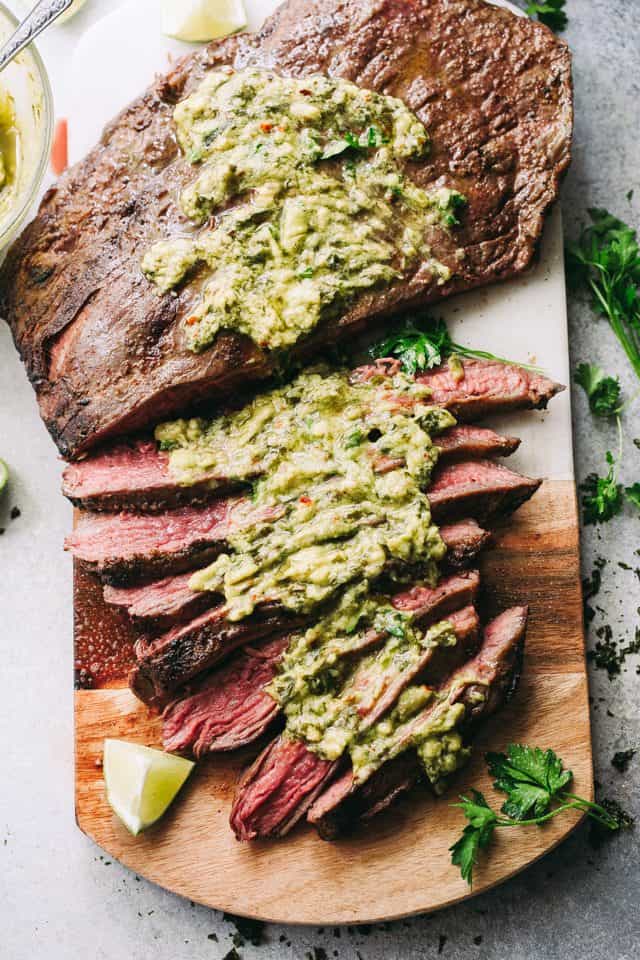 Grilled flank steak with chimichurri sauce on a cutting board.