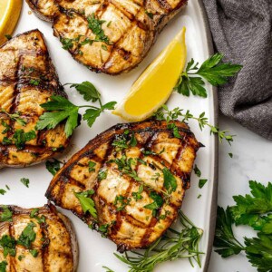 four grilled swordfish steaks on a serving platter with lemon wedges