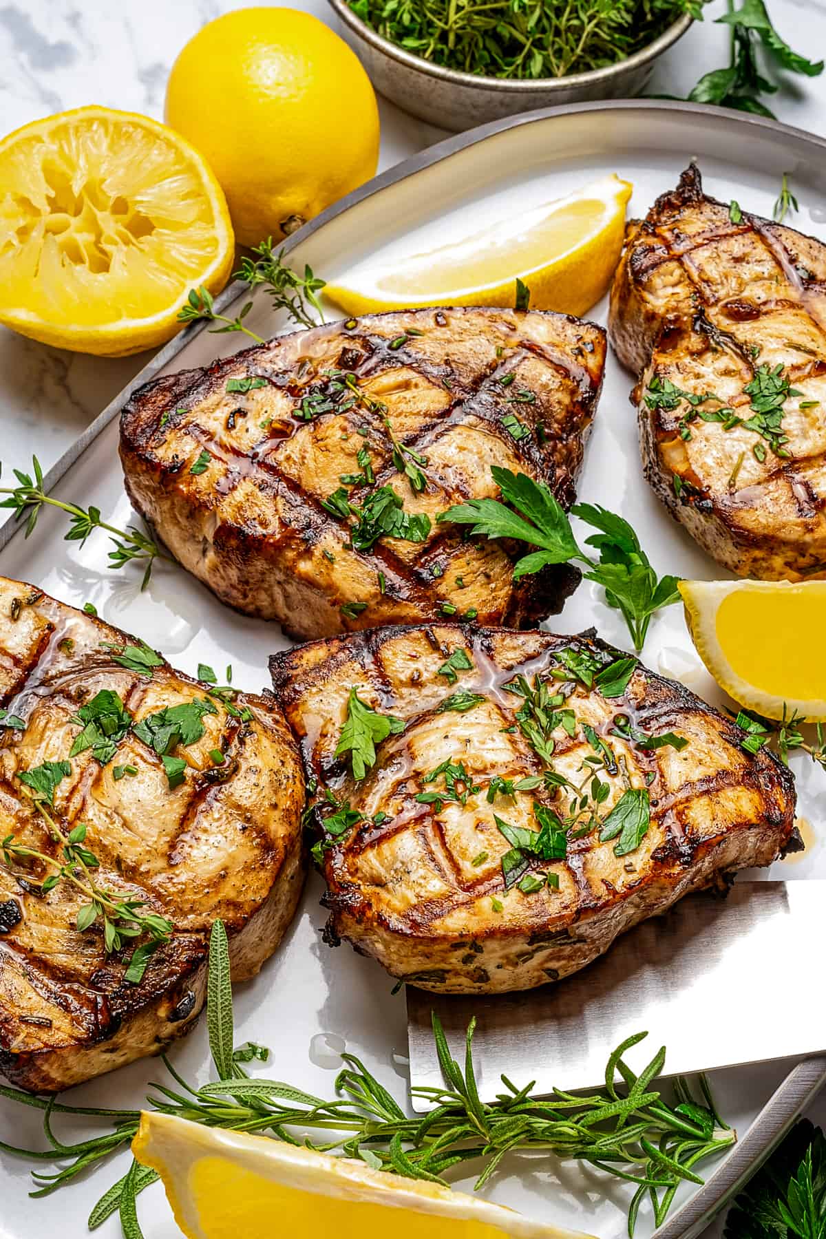 four grilled swordfish steaks on a serving platter with lemon wedges