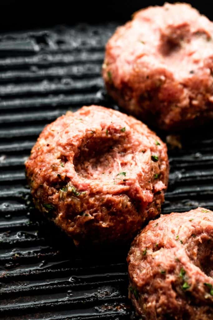 black grill with three ground turkey patties with thumb indentation in the center of each patty.