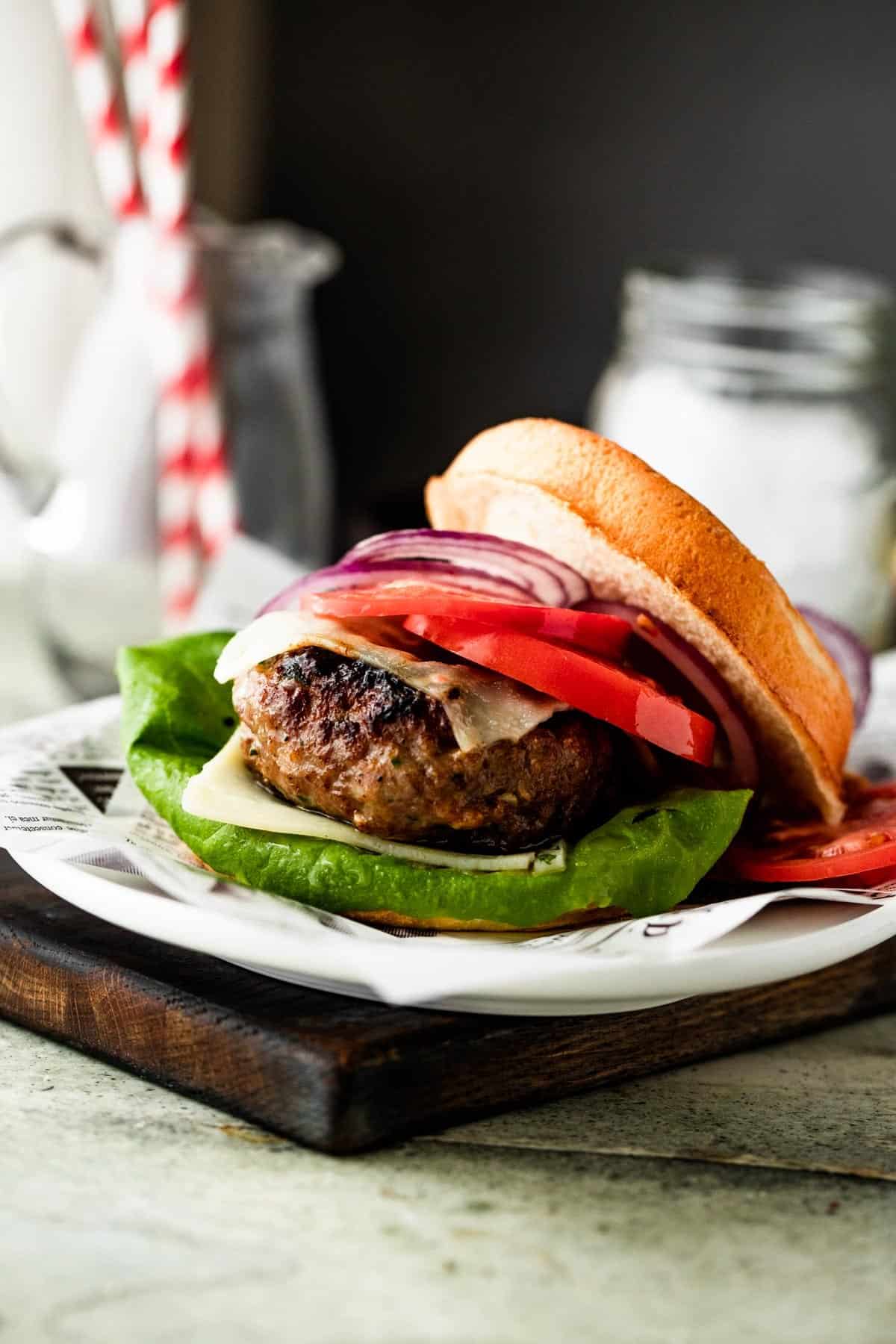 shot of a grilled turkey burger dressed with tomato slices, cheese slices, red onion slices, and green salad.