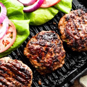 three turkey burgers on a black backdrop with lettuce, tomatoes, and red onion slices arranged alongside the burgers.