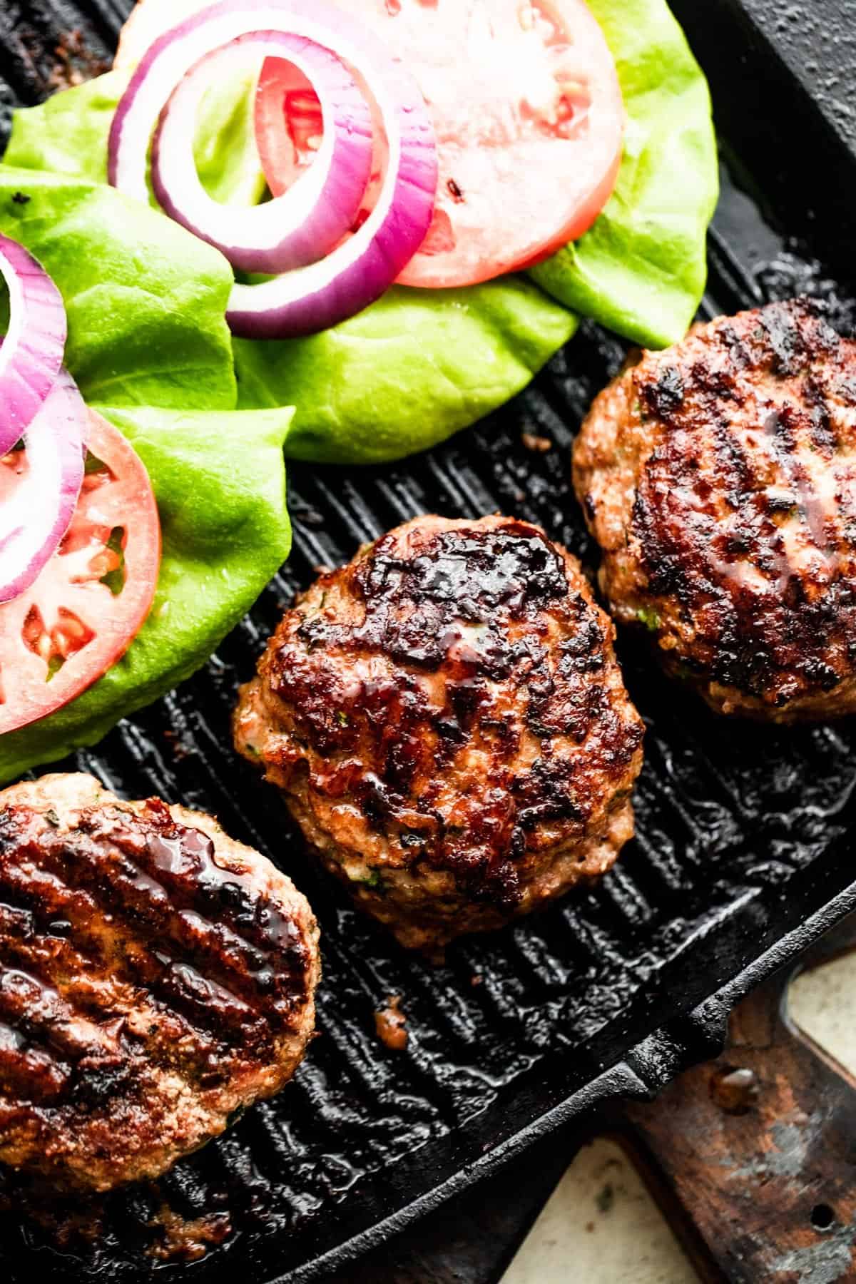 three turkey burgers on a black backdrop with lettuce, tomatoes, and red onion slices arranged alongside the burgers.