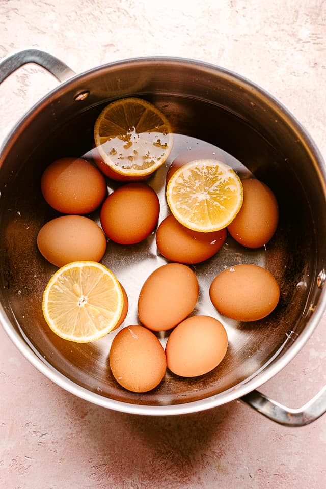 Boiling brown eggs in a pot with three lemon slices.